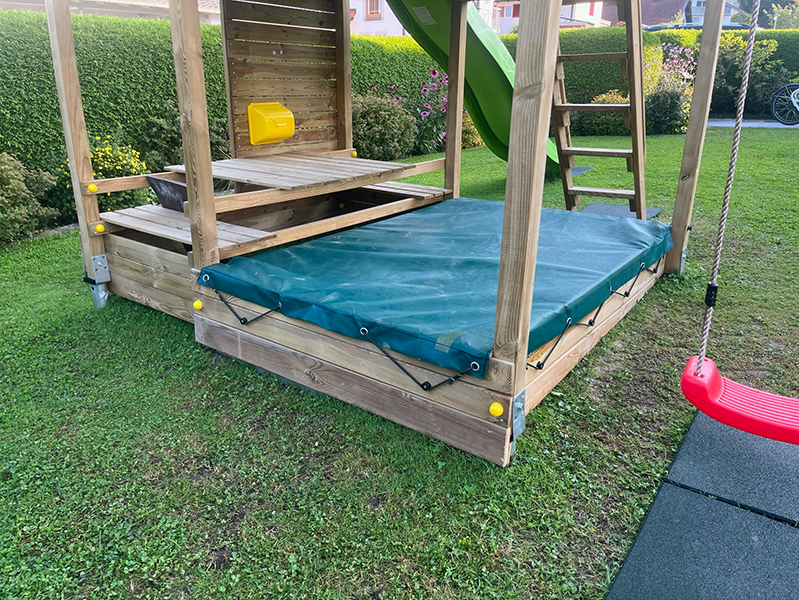 Gummierte Sandkastenabdeckung mit Aussparungen und Gummiseil zum Befestigen.